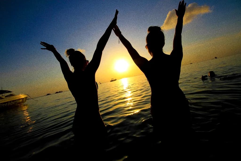 Two people throwing their arms up in shallow water at sunset