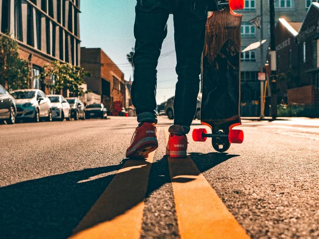 Feet on a skateboard casting a long shadow across sunlit tarmac