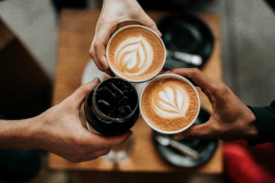 Three hands bringing coffee cups together over a table
