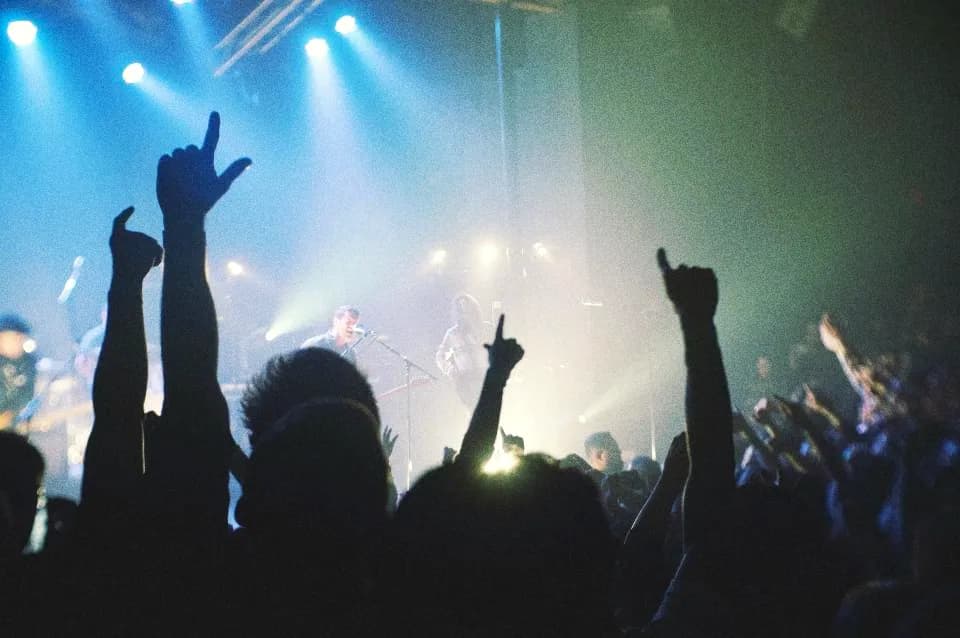 Silhouetted crowd with arms up in front of a bright stage