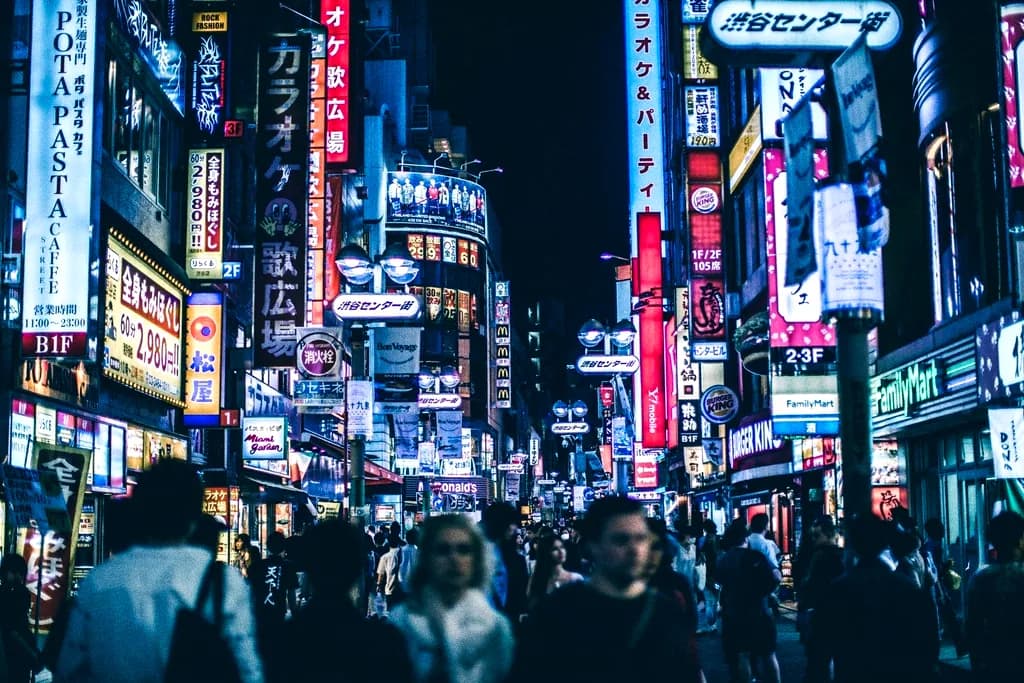 A dense crowd moving down a narrow street packed with glowing signs