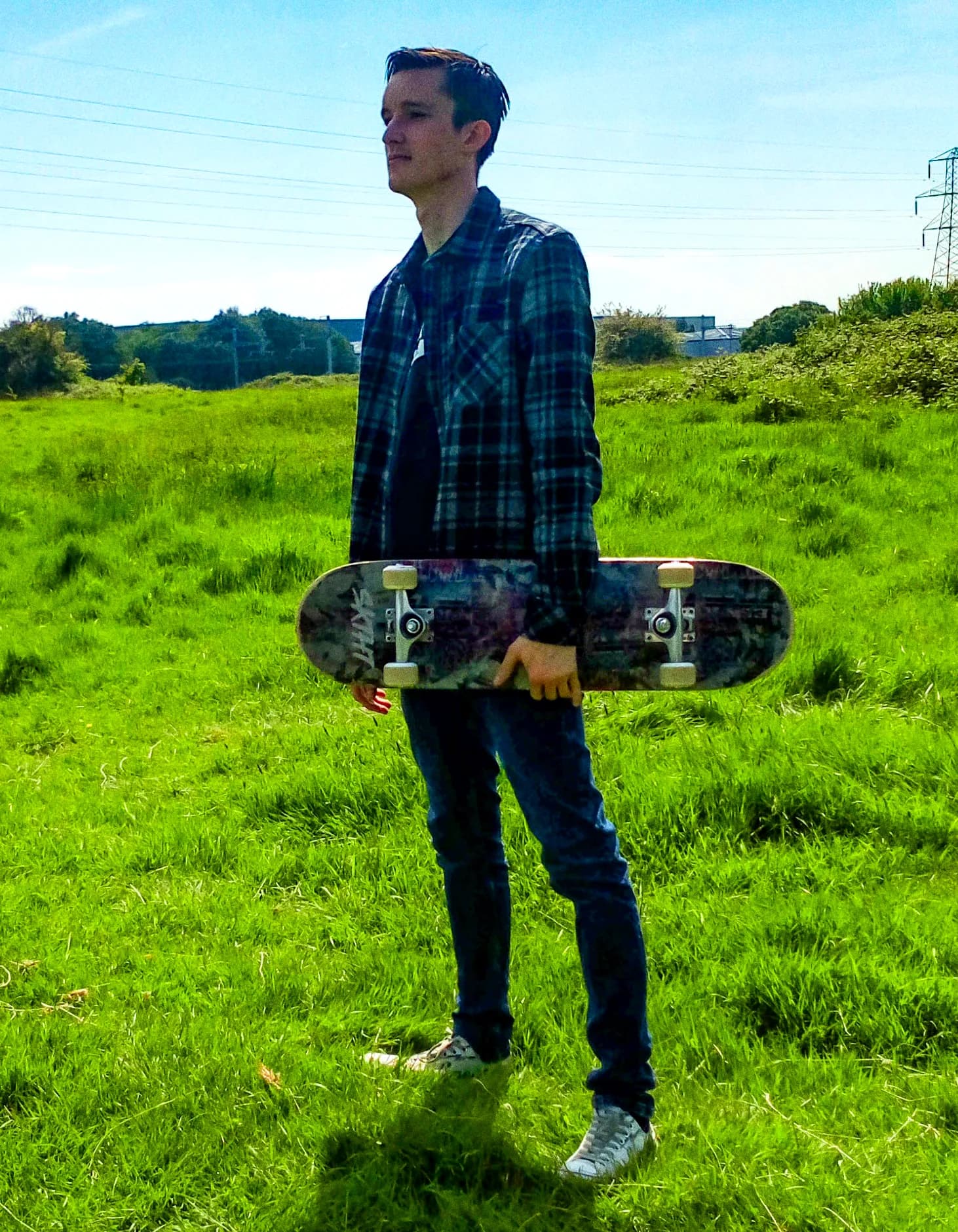 Someone carrying a skateboard across an open green field