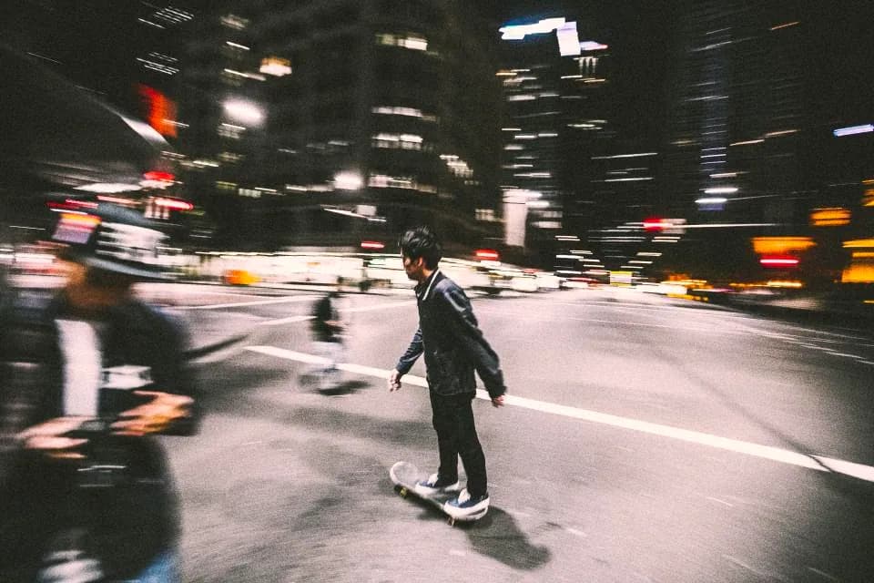 A skateboarder rolling through a dark street, motion blurred