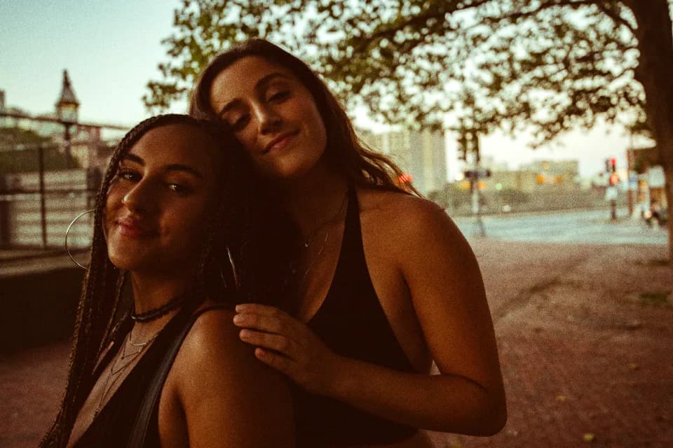 Two friends leaning their heads together, laughing in golden evening light